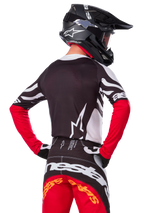 Piloto de motocross visto de costas a usar a camisola Alpinestars Limited Edition Techstar Deep, em preto, branco e vermelho vivo, com calças de corrida a condizer e um capacete preto, ajuste atlético para performance em todo-o-terreno