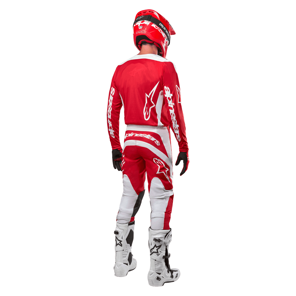 Vista traseira de um piloto de motocross a usar a Camisola Alpinestars 2024 Fluid Lurv em Vermelho Mars e Branco, combinada com calças vermelhas e brancas a condizer, botas de todo-o-terreno brancas e um capacete vermelho, mostrando o design das costas da camisola e o logótipo Alpinestars.