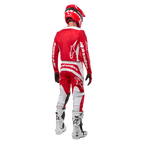 Vista traseira de um piloto de motocross a usar a Camisola Alpinestars 2024 Fluid Lurv em Vermelho Mars e Branco, combinada com calças vermelhas e brancas a condizer, botas de todo-o-terreno brancas e um capacete vermelho, mostrando o design das costas da camisola e o logótipo Alpinestars.