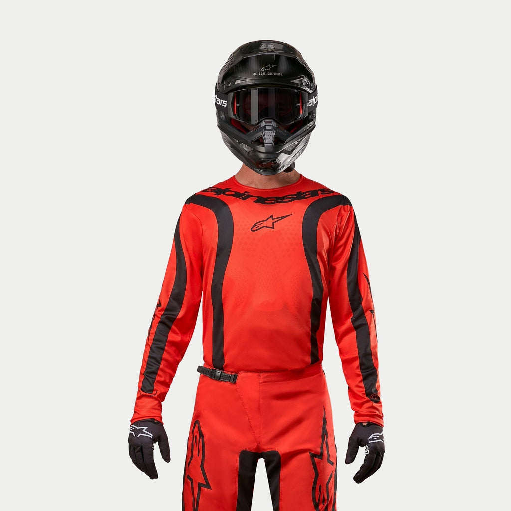 Piloto de motocross a usar a camisola Alpinestars 2024 Fluid Lurv, em laranja e preto, calças de motocross a condizer, capacete preto com óculos e luvas pretas, equipamento coordenado para corridas de todo-o-terreno