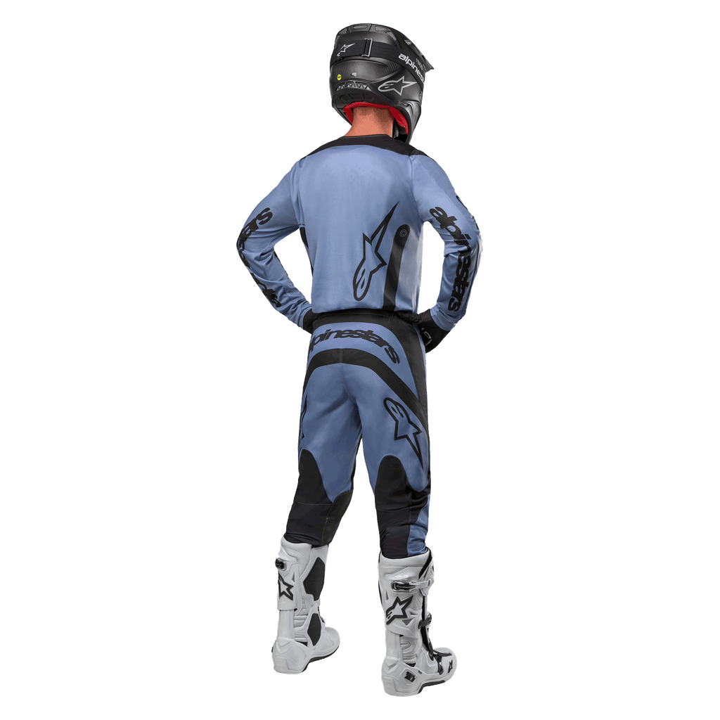 Piloto de motocross visto de costas a usar a camisola Alpinestars 2024 Fluid Lurv e calças a condizer em azul claro e preto, com logótipos pretos nas costas e mangas, acompanhado por capacete preto e botas brancas