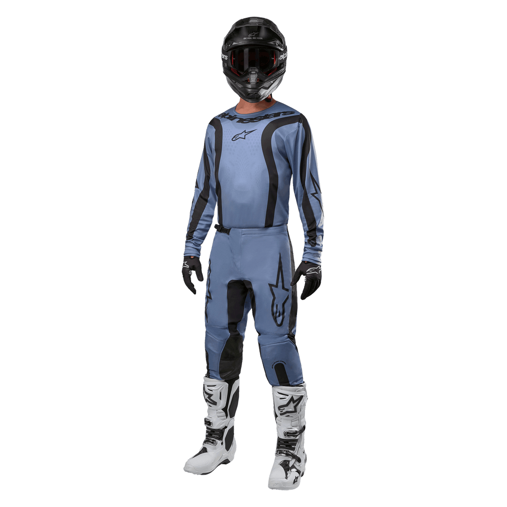 Piloto de motocross com equipamento de competição completo, camisola Alpinestars 2024 Fluid Lurv em azul claro e preto, calças em azul claro a condizer com painéis pretos, botas brancas e pretas, luvas pretas e capacete preto com óculos, conjunto coordenado para corridas todo-o-terreno