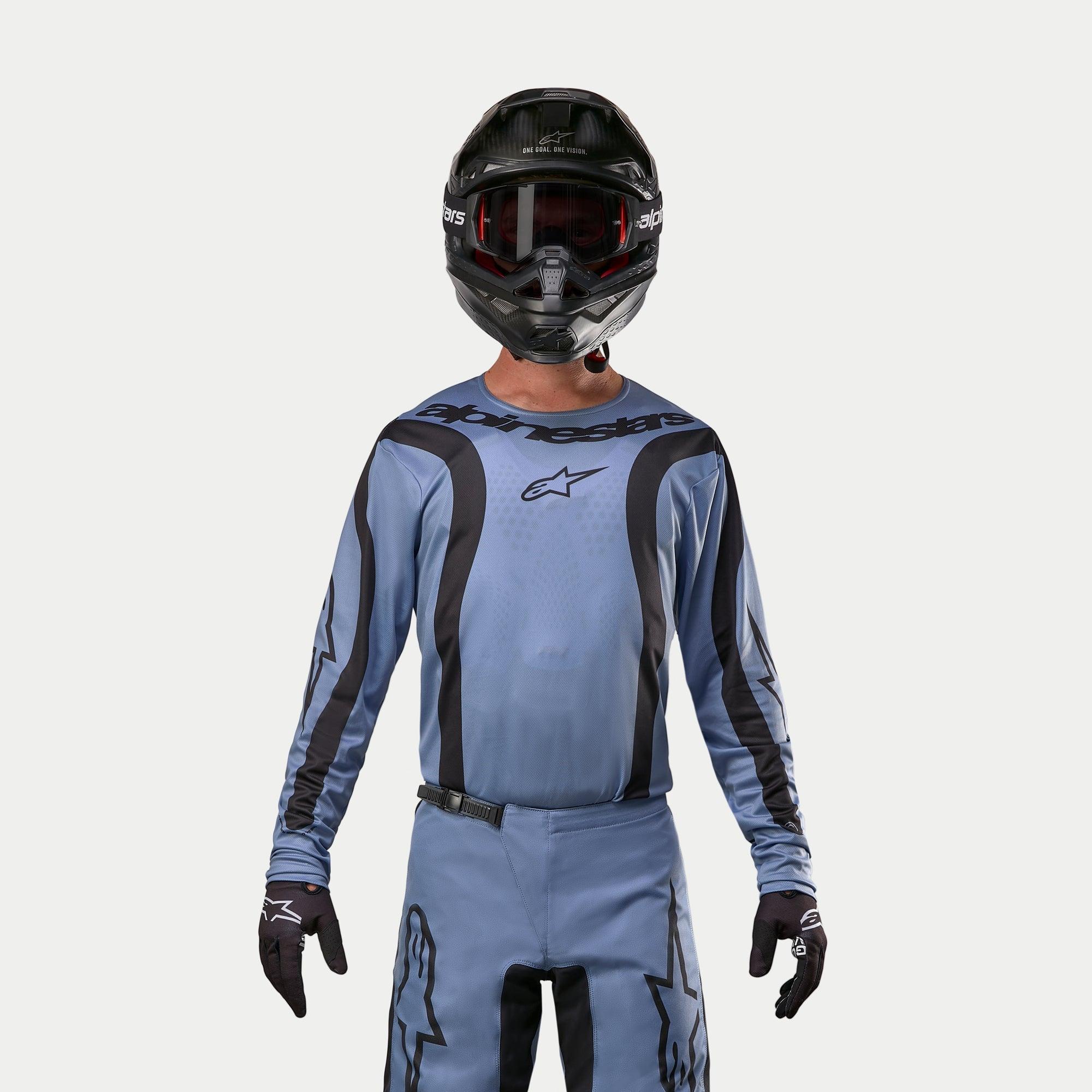 Alpinestars 2024 Fluid Lurv Jersey, camisola de motocross, azul claro e preto, usada por um piloto com calças a condizer, capacete preto com óculos vermelhos e luvas pretas, conjunto coordenado para corridas todo-o-terreno