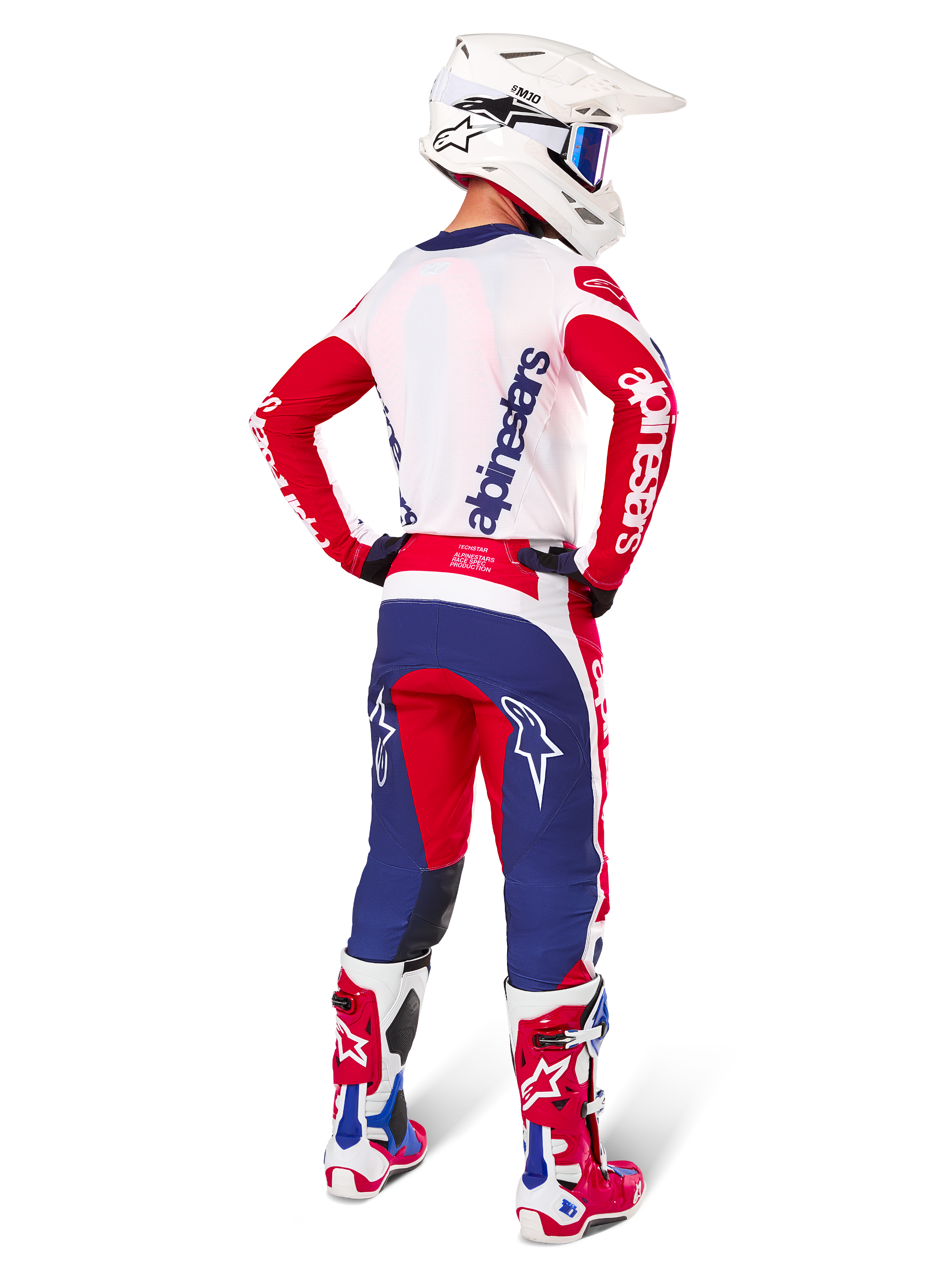 Motocross rider seen from the back wearing the Alpinestars Limited Edition Techstar Fortitude Jersey and Gear Set, Bright Red White and Blue colorway, featuring white Alpinestars branding on red sleeves and a navy logo on the white back, paired with a white motocross helmet and matching racing boots.