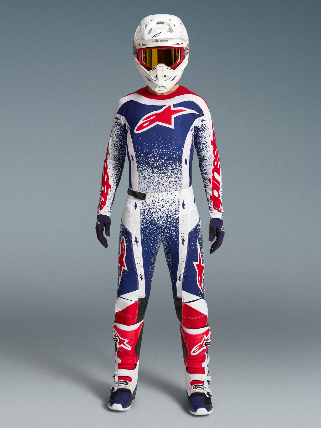 Alpinestars Techstar Unity Jersey Edição Limitada, camisola de motocross para homem, azul, branca e vermelha com gráficos salpicados, vista frontal em conjunto de equipamento de todo-o-terreno.