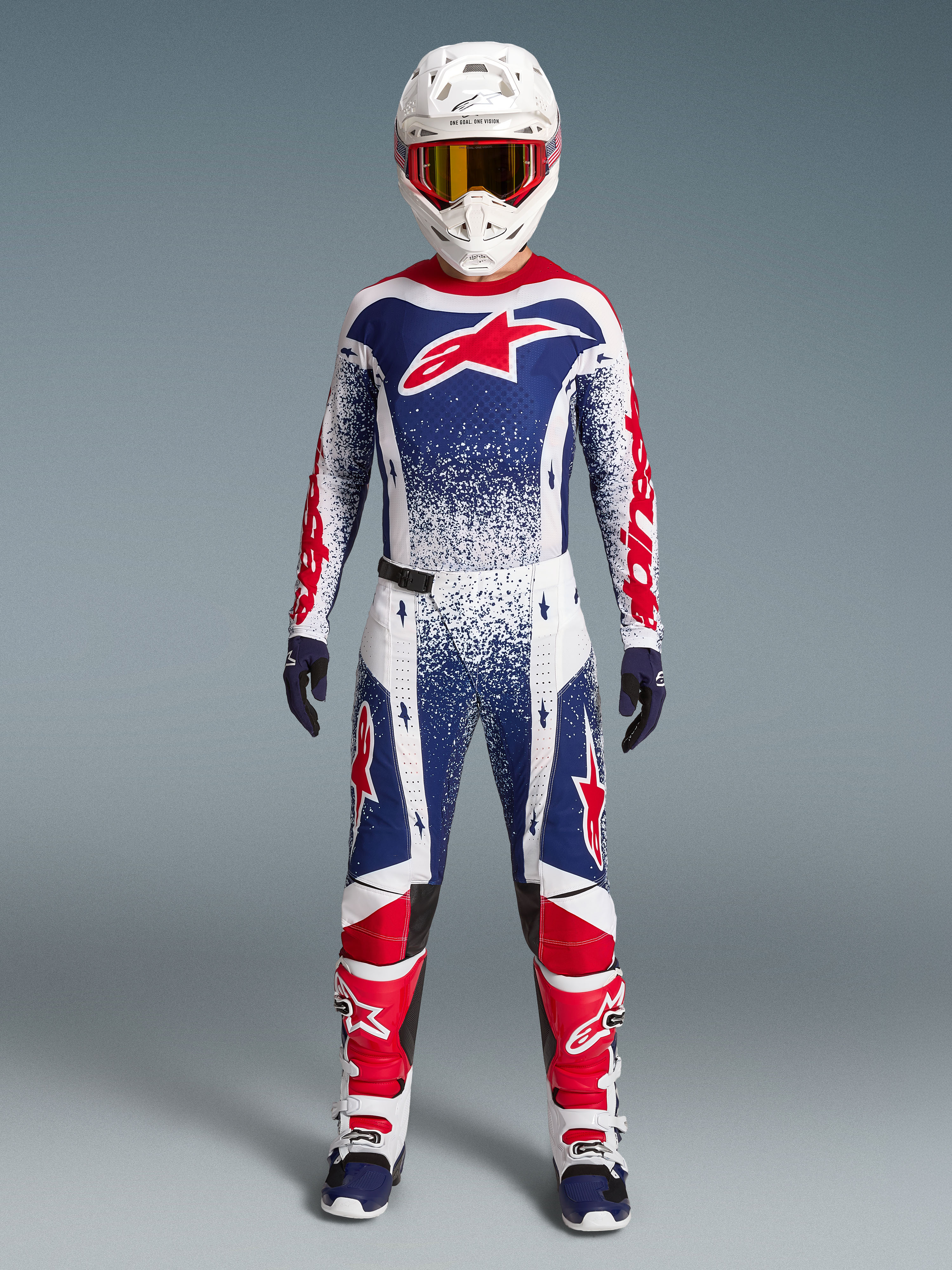 Alpinestars Techstar Unity Jersey Edição Limitada, camisola de motocross para homem, azul, branca e vermelha com gráficos salpicados, vista frontal em conjunto de equipamento de todo-o-terreno.