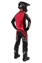 Piloto de motocross visto de costas a usar a camisola 2024 Supertech Ward em Black Red Berry, com um painel traseiro vermelho vibrante e mangas pretas com a marca Alpinestars a branco. Combinado com calças de motocross a condizer, botas Tech 10 pretas e um capacete de fibra de carbono preto para um conjunto de equipamento de corrida profissional coordenado.