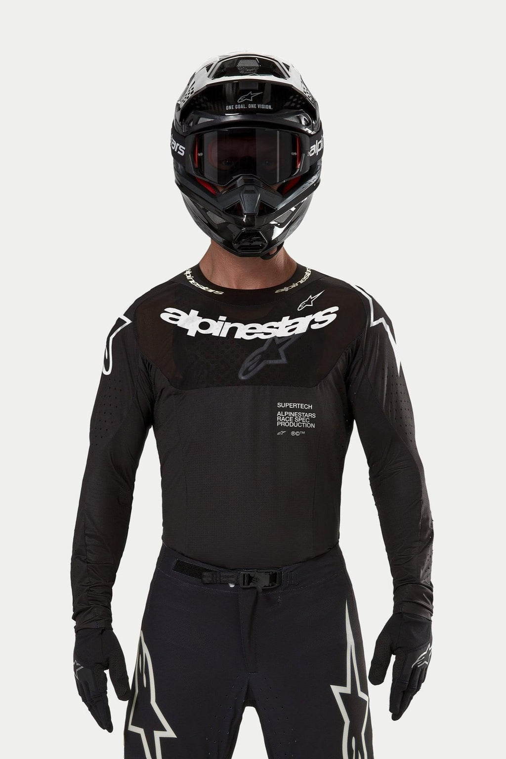 Piloto de motocross a usar a camisola Alpinestars Supertech Ward 2024 em preto, corte atlético de corrida com logótipo Alpinestars branco no peito, apresentando perfurações cortadas a laser e o texto 'Supertech Race Spec', combinada com um capacete preto e óculos para corridas todo-o-terreno.