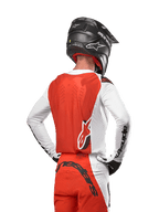 Camisola Alpinestars Supertech Ward 2024 em White Hot Orange, vista traseira de um piloto de motocross, painel traseiro laranja e mangas brancas com logótipo preto, calças a condizer e capacete preto, equipamento profissional para off-road