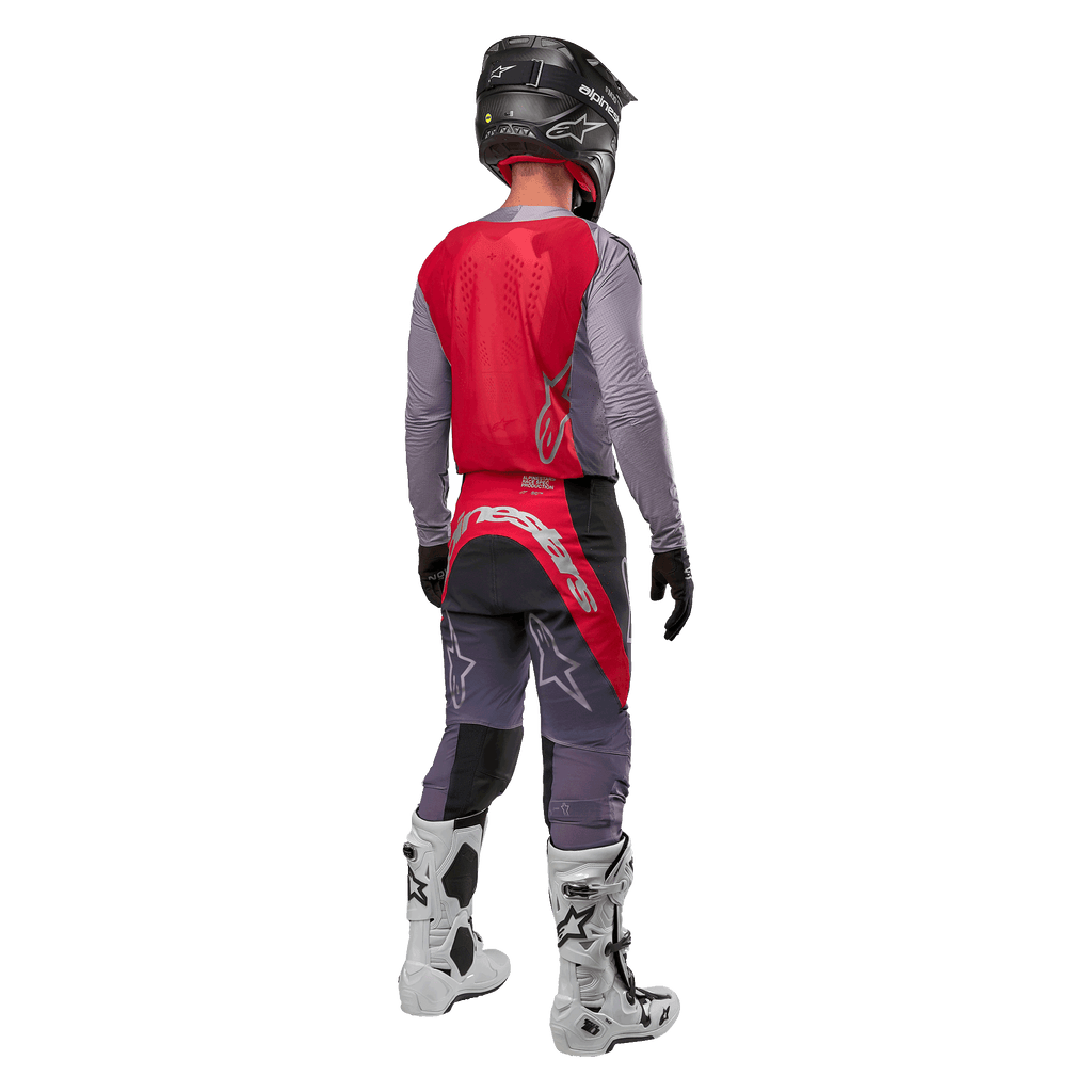 Alpinestars 2024 Supertech Dade Jersey, camisola de motocross, vermelho Iron Red Berry e cinzento, vista traseira num piloto, com painel traseiro vermelho, logótipo cinzento e mangas cinzentas, usada com calças de corrida coordenadas em cinzento e vermelho, botas brancas e capacete preto, equipamento profissional de todo-o-terreno.