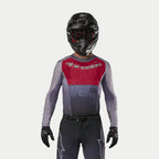 Piloto de motocross a usar a camisola Alpinestars 2024 Supertech Dade em Iron Red Berry, com um painel vermelho no peito e mangas cinzentas com logótipo prateado, usada com calças a condizer, capacete preto e luvas pretas, equipamento profissional de corrida off-road