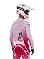 Piloto de motocross visto de costas a usar a camisola Alpinestars 2024 Supertech Dade em Red Berry Lilac, com painéis em malha respirável e logótipos Alpinestars vermelhos, combinada com calças em vermelho e lilás a condizer e um capacete Alpinestars branco com óculos, equipamento profissional de corrida todo-o-terreno
