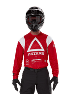 Piloto de motocross a usar a Camisola Alpinestars Techdura em vermelho vivo com gráficos brancos, apresentando um grande triângulo branco e o logótipo ASTARS no peito, combinada com capacete, óculos e equipamento de condução em preto, um conjunto coordenado para enduro e corridas de todo-o-terreno