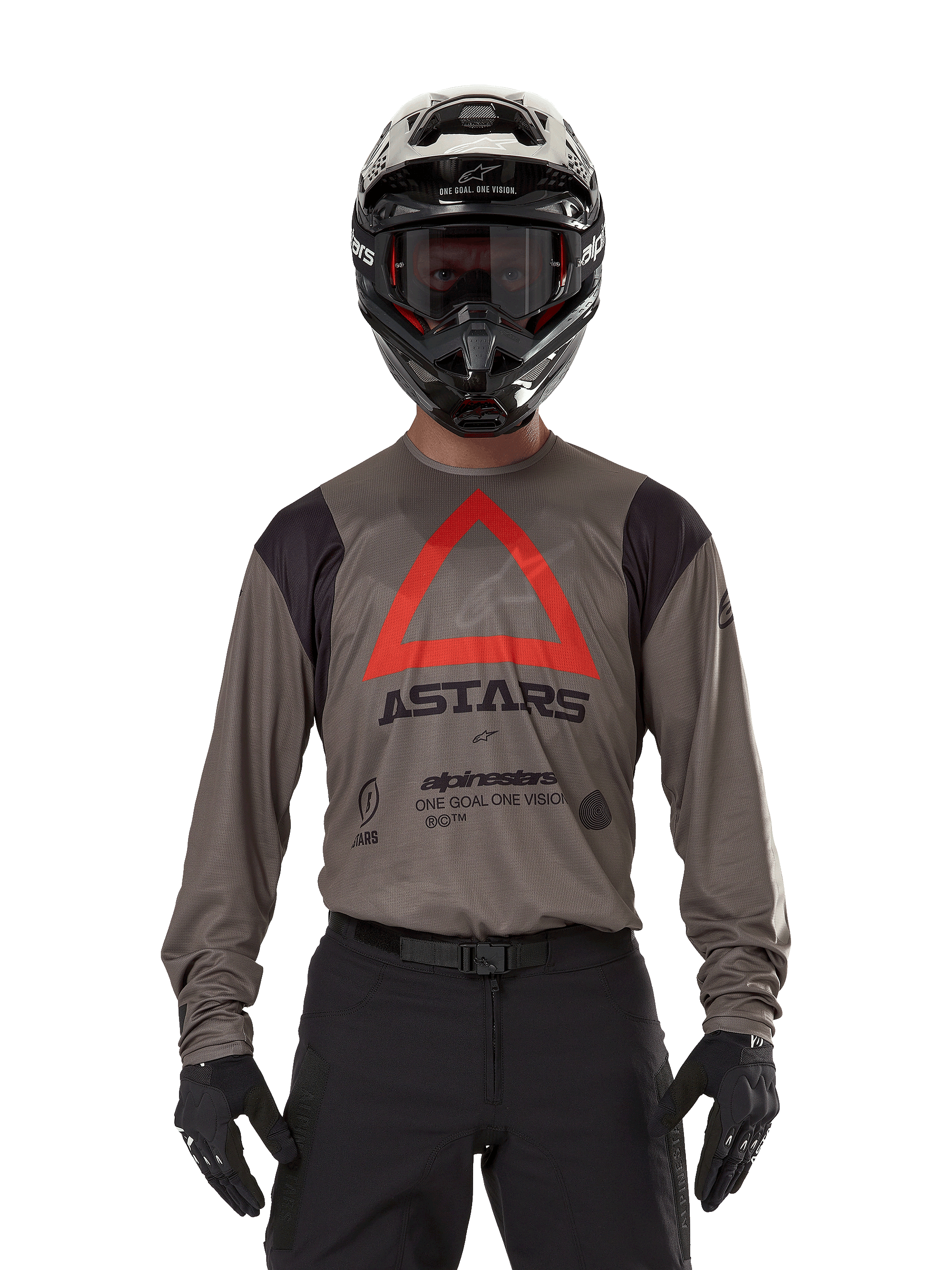 Piloto de motocross a usar a Camisola Alpinestars Techdura em Falcon Brown, com um triângulo vermelho proeminente e a marca 'ASTARS' no peito, acompanhada de calças pretas, capacete preto com óculos e luvas pretas, equipamento completo de corrida enduro