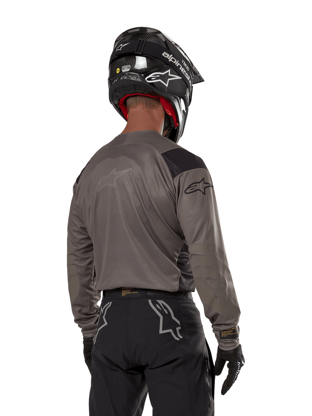 Piloto de motocross visto de costas a usar a camisola Alpinestars Techdura em Falcon Brown, combinada com calças de off-road pretas e um capacete preto, com um design gráfico moderno e parte traseira alongada para a prática de enduro