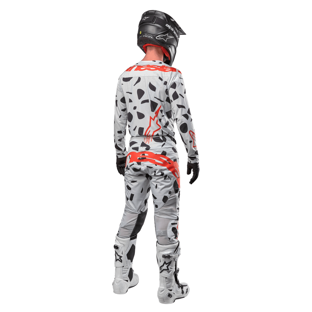 Piloto de motocross visto de costas a usar camisola Alpinestars 2024 Techstar Rantera e calças a condizer, padrão Haze Gray Camo com logótipos Alpinestars vermelhos destacados, capacete preto, botas brancas e pretas, luvas pretas, conjunto de equipamento de motocross coordenado