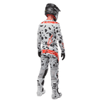Piloto de motocross visto de costas a usar camisola Alpinestars 2024 Techstar Rantera e calças a condizer, padrão Haze Gray Camo com logótipos Alpinestars vermelhos destacados, capacete preto, botas brancas e pretas, luvas pretas, conjunto de equipamento de motocross coordenado