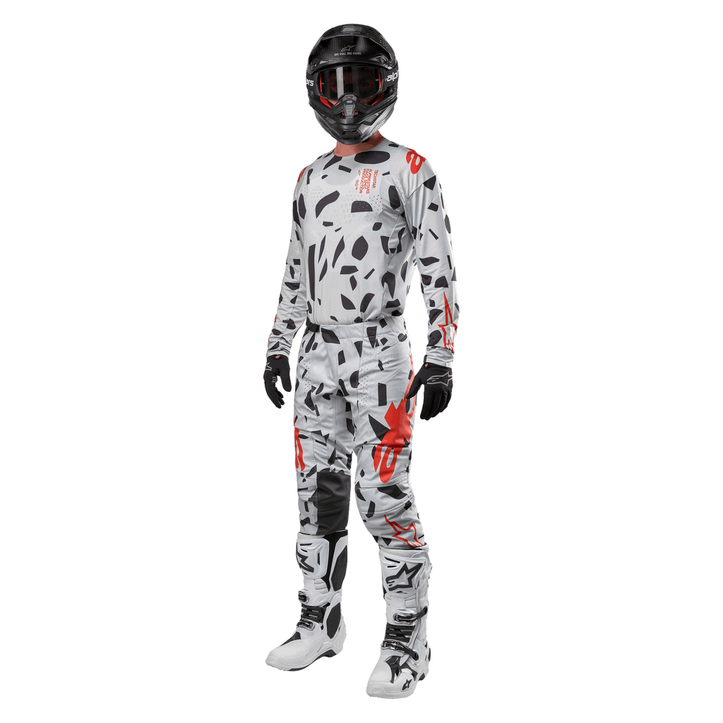 Piloto de motocross com camisola Alpinestars 2024 Techstar Rantera em Haze Gray Camo, calças a condizer com detalhes em vermelho e preto, capacete e óculos pretos, luvas pretas, botas brancas e pretas, equipamento completo de motocross para performance todo-o-terreno