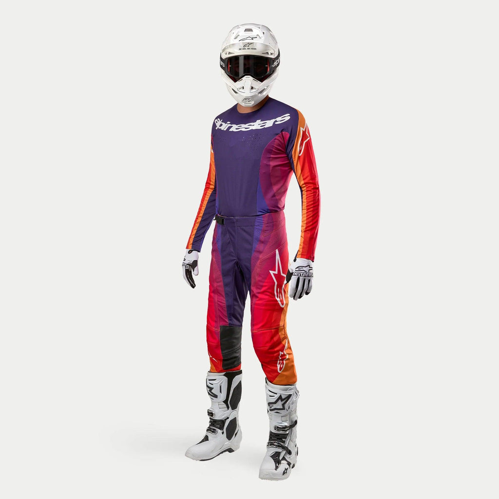 Equipamento completo de motocross Alpinestars, incluindo a camisola e calças 2024 Techstar Pneuma em roxo escuro, laranja e azul profundo, capacete branco, óculos de proteção, luvas brancas e pretas, e botas brancas com detalhes pretos, kit de alta performance.
