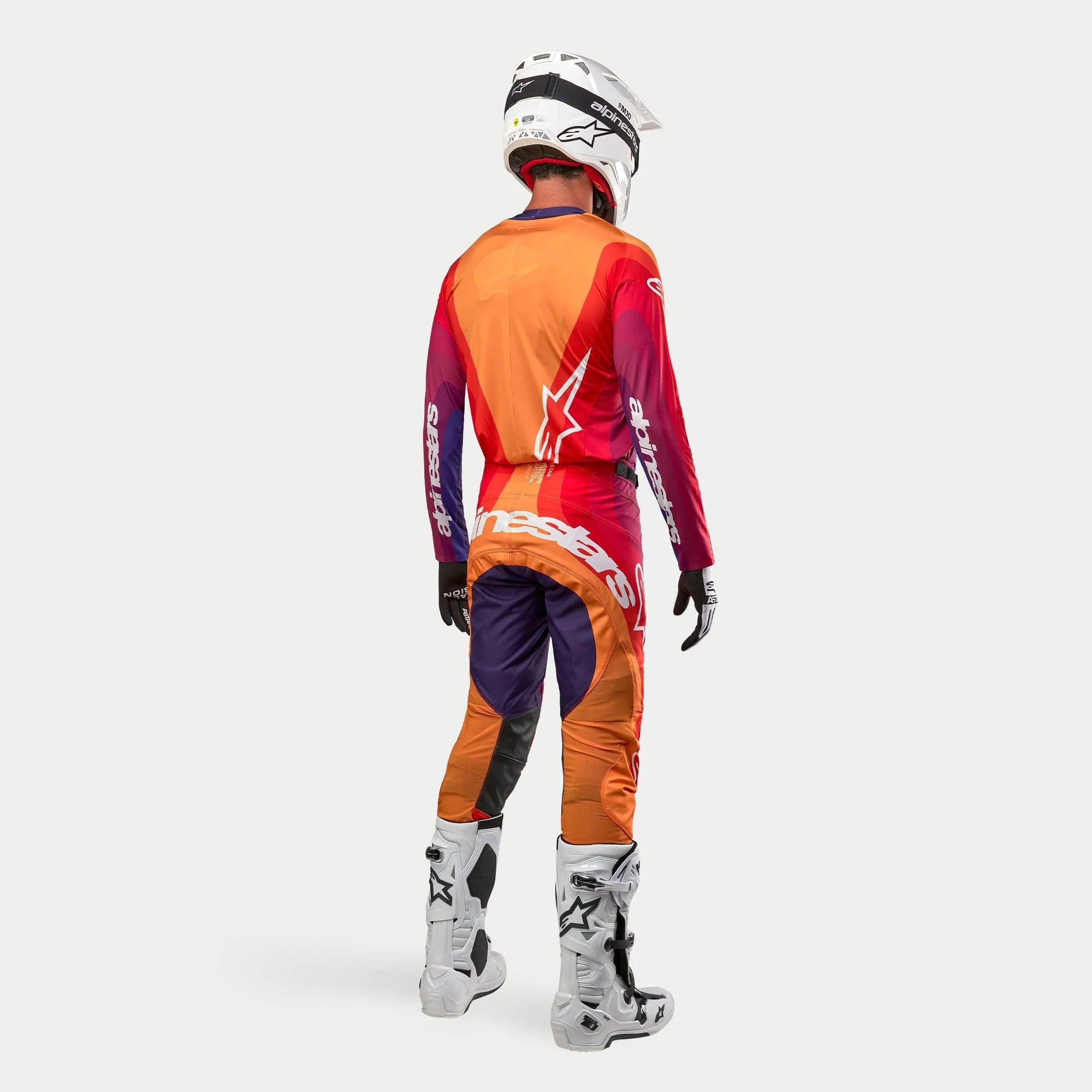 Equipamento completo de motocross Alpinestars Techstar Pneuma, visto de costas, incluindo camisola e calças em tons de roxo, laranja e vermelho com logótipos brancos, botas de motocross brancas e capacete branco.