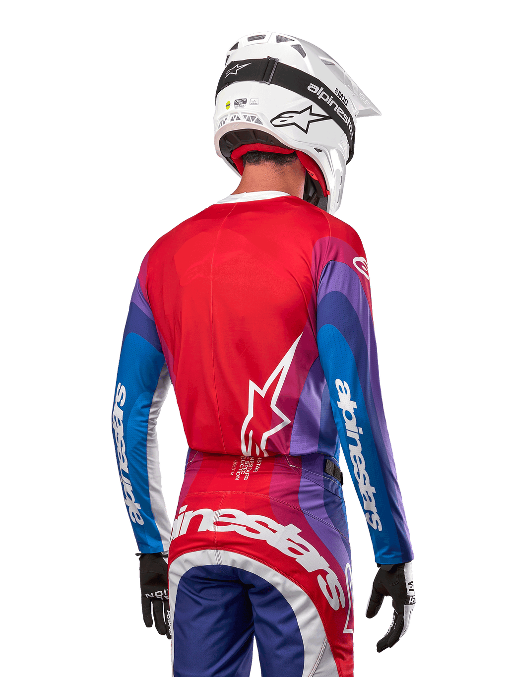 Piloto de motocross visto de costas a usar a camisola Alpinestars 2024 Techstar Pneuma em azul, vermelho e branco, com as costas vermelhas e logótipo de estrela branco, mangas azuis e roxas com a marca a branco, coordenada com calças a condizer e um capacete branco para corridas todo-o-terreno.