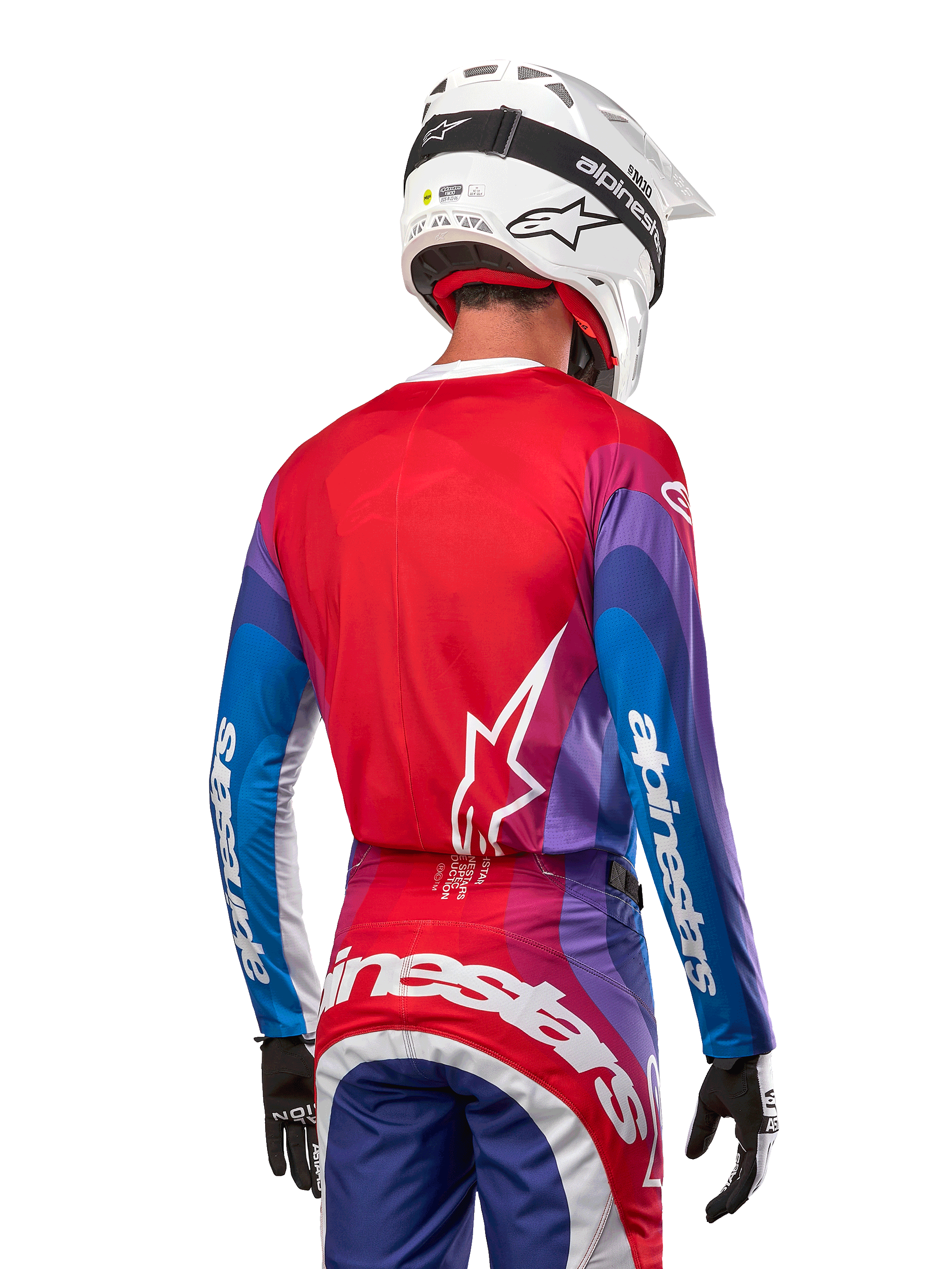 Piloto de motocross visto de costas a usar a camisola Alpinestars 2024 Techstar Pneuma em azul, vermelho e branco, com as costas vermelhas e logótipo de estrela branco, mangas azuis e roxas com a marca a branco, coordenada com calças a condizer e um capacete branco para corridas todo-o-terreno.