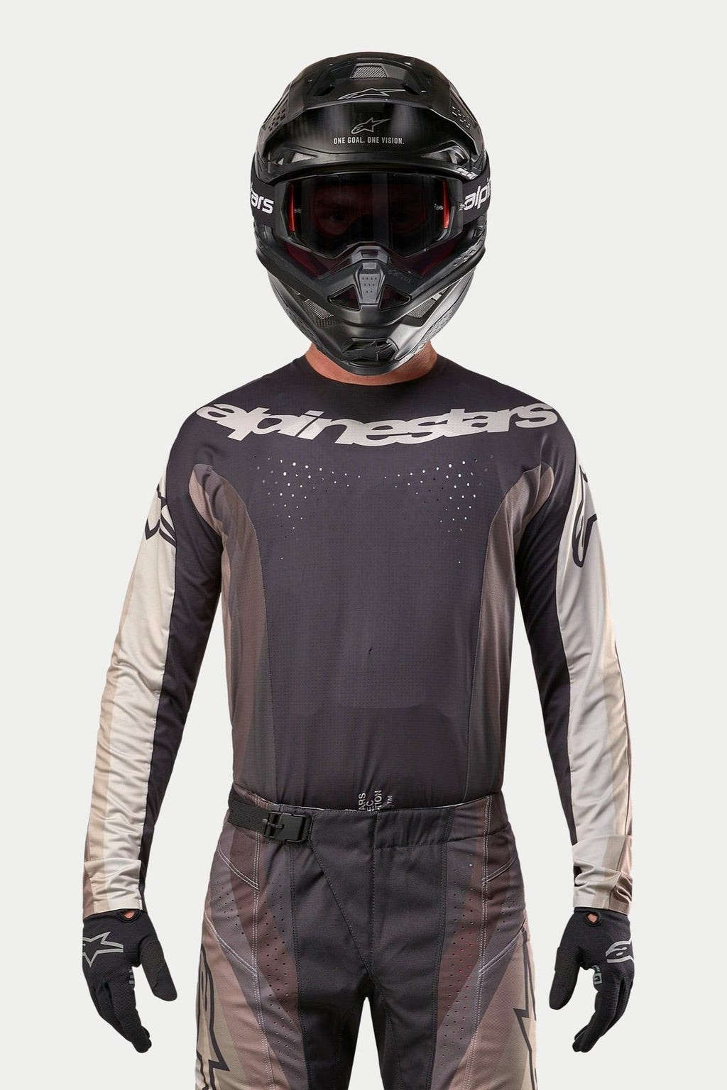 Camisola Alpinestars 2024 Techstar Pneuma, camisola de motocross, Dark Sand e cinzento Iron Dust Gray, usada com calças de motocross a condizer e um capacete preto, com um logótipo Alpinestars proeminente no peito e perfurações de ventilação cortadas a laser, equipamento de corrida off-road de alta performance.