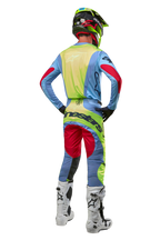 Motocross rider from the back wearing the Alpinestars 2024 Techstar Ocuri Jersey, Light Blue with Yellow Fluo and Red Berry accents, matching racing pants, white boots, and neon helmet, complete off-road gear for professional competition