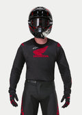 Motocross rider wearing the Alpinestars Honda Racer Iconic Jersey in Black and Red, featuring a large red Honda wing logo on the chest and white Astar logo, paired with a matching black helmet, goggles, and gloves for a complete off-road racing kit