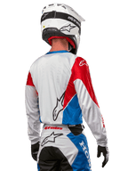 Motocross rider wearing the Alpinestars Honda Racer Iconic Jersey, back view, White with Bright Blue and Bright Red panels, featuring prominent Alpinestars logo on the back, paired with a white motocross helmet and matching racing pants.