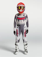 Alpinestars Supertech Swan 2027 para jovens, conjunto de motocross cinzento e branco com pormenores vermelhos.