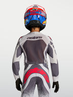 Alpinestars Juventude Supertech Swan, camisola e calças de motocross, cinzento e branco com pormenores vermelho fluo, vista traseira no piloto.