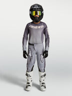 Alpinestars Juventude Fluid Amber Gear Set, conjunto de motocross cinzento e areia para jovens, com capacete e botas brancas.