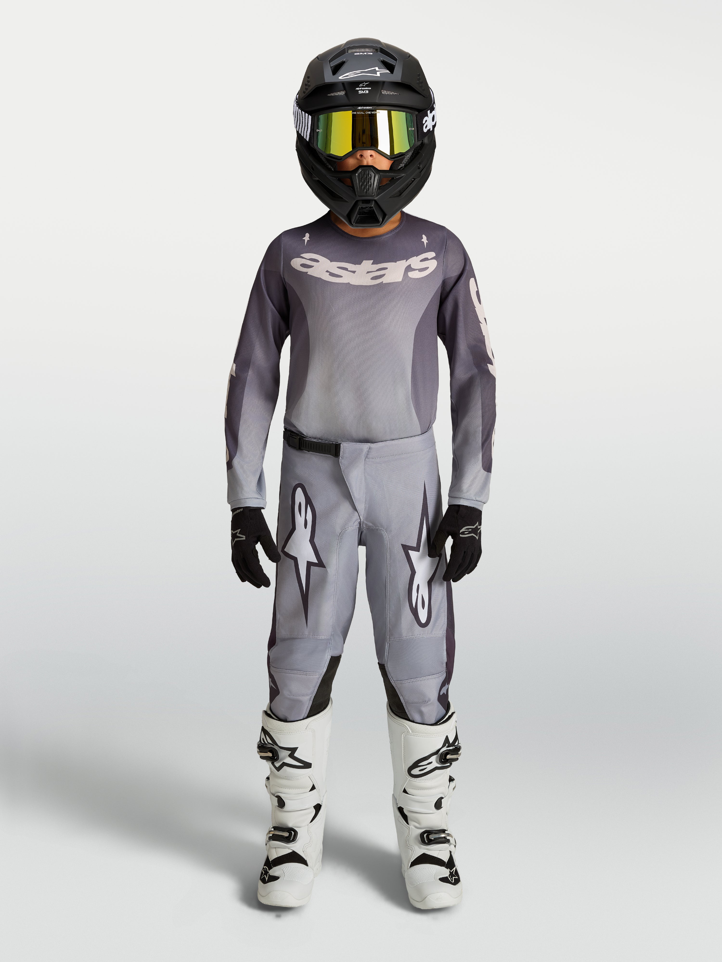 Alpinestars Juventude Fluid Amber Gear Set, conjunto de motocross cinzento e areia para jovens, com capacete e botas brancas.