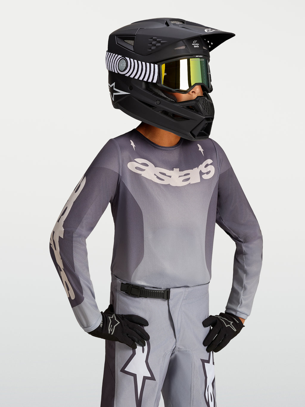 Alpinestars camisola Fluid Amber Jovem 2027, camisola de motocross em cinzento e areia com capacete de corrida preto.