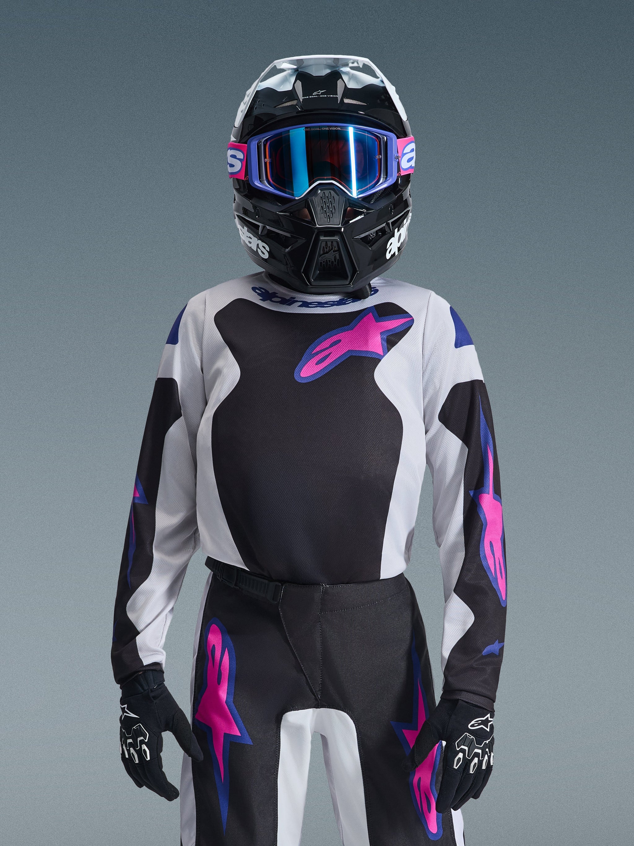 Young motocross rider wearing the Alpinestars 2026 Youth Fluid Grid Jersey in Black, Light Gray, and Purple, paired with matching grid-patterned pants, black helmet with blue-lensed goggles, and black gloves, complete gear set for youth off-road racing.