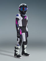 Young motocross rider wearing the Alpinestars 2026 Youth Fluid Grid Jersey in black, light gray, and purple, featuring pink star logos on the chest and sleeves. The outfit is paired with matching motocross pants, a black helmet with blue-tinted goggles, and black and white boots, representing a complete off-road racing kit for youth.