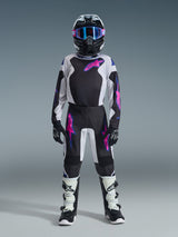 Young motocross rider wearing the Alpinestars 2026 Youth Fluid Grid Jersey in Black, Light Gray, and Purple, paired with matching motocross pants, black helmet with pink accents and blue goggles, black and white boots, and black gloves, complete professional off-road racing gear set