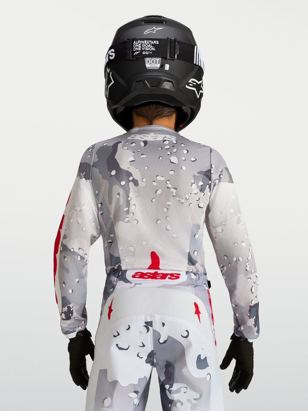 Alpinestars Camisola Fluid Lone Jovem 2027, camisola de motocross para jovem, cinzenta camuflada com detalhes vermelhos, vista traseira com capacete preto.