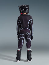 Jovem piloto de motocross visto de costas a usar a camisola 2026 Youth Fluid Apex em preto e cinzento, calças de motocross a combinar com grandes grafismos do logótipo em branco, capacete preto e botas Tech Series pretas e brancas, conjunto completo de equipamento de performance para condução todo-o-terreno.