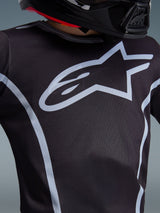 Alpinestars 2026 Youth Fluid Apex Jersey, pormenor do design no peito, preto e cinzento, com um logótipo de estrela cinzento claro proeminente e linhas de contorno atléticas, usada com um capacete preto, equipamento de motocross de performance para jovens pilotos