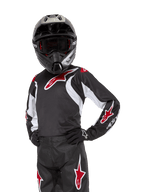 Camisola Racer Lucent Jovem 2024, camisola de motocross, preta, branca e vermelha, usada por um jovem piloto com capacete preto e calças a condizer, com logótipos de estrelas vermelhas e detalhes gráficos brancos, vestuário de performance para motocross e todo-o-terreno
