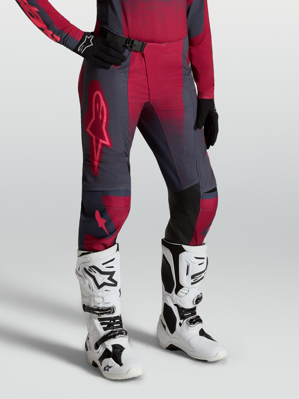 Alpinestars Stella Techstar Swan, calças de motocross para mulher, cinzentas e vermelhas, usadas com botas brancas.