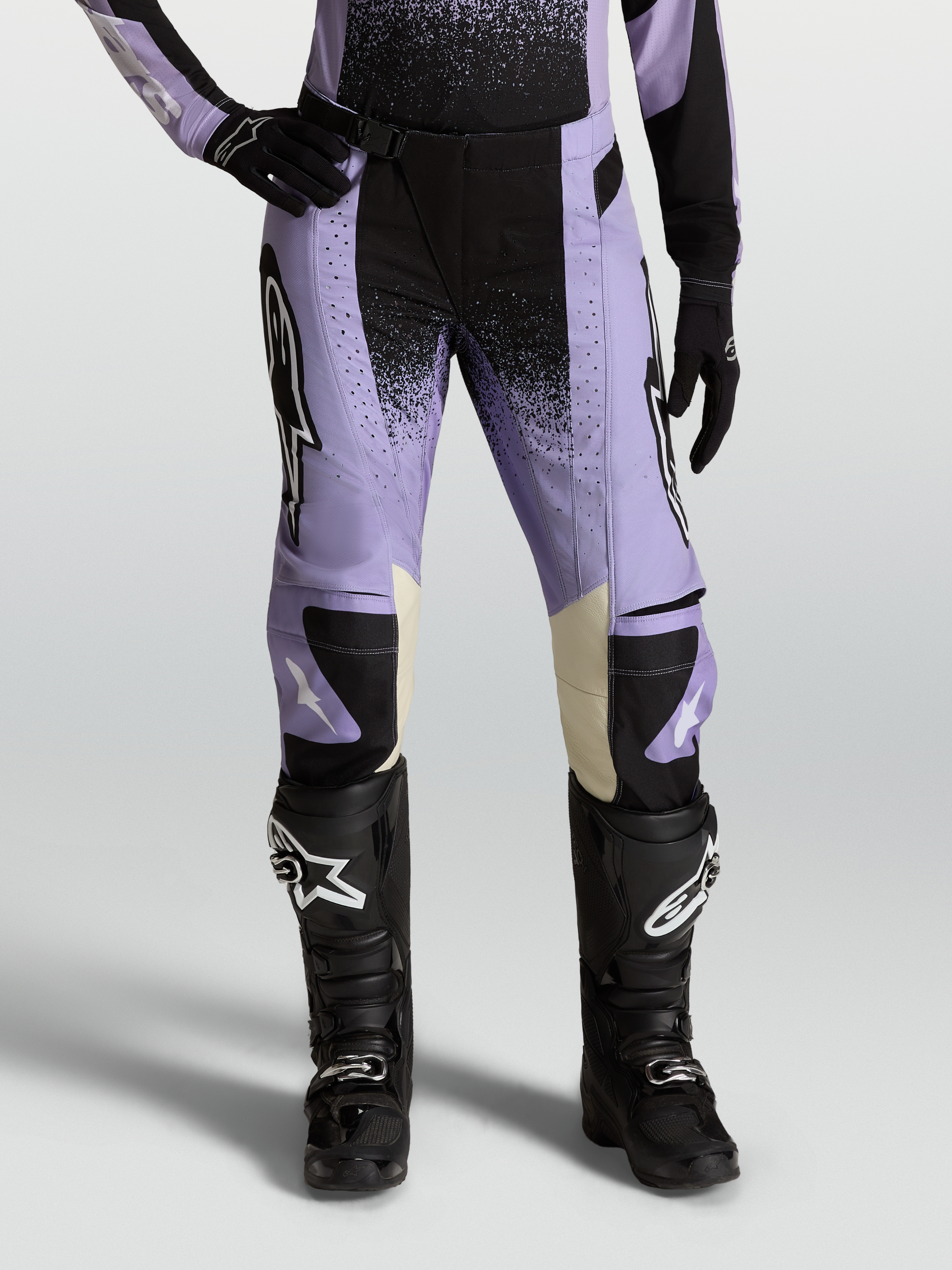 Alpinestars Stella Techstar Swan, calças de motocross para mulher, roxo claro e preto com pormenores em pele creme, combinadas com botas off-road pretas.