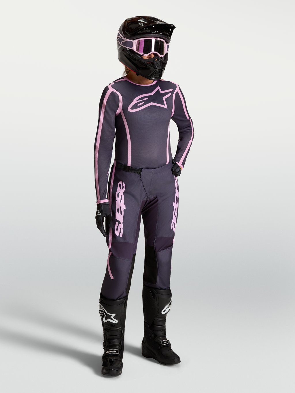 Alpinestars Stella Fluid Apex V2, conjunto de motocross para mulher, cinzento e rosa, com botas de moto pretas e capacete.