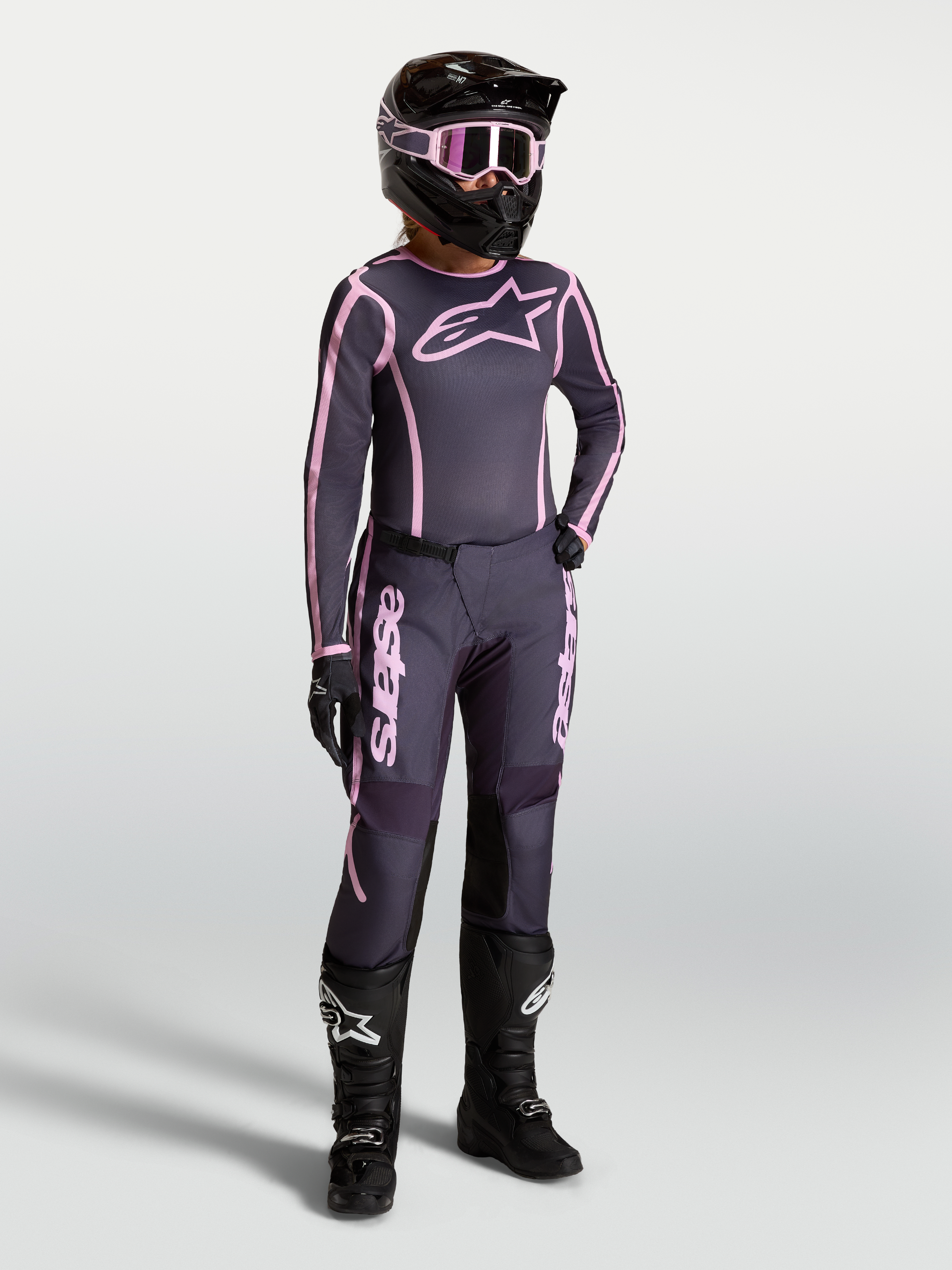 Alpinestars Stella Fluid Apex V2, conjunto de motocross para mulher, cinzento e rosa, com botas de moto pretas e capacete.