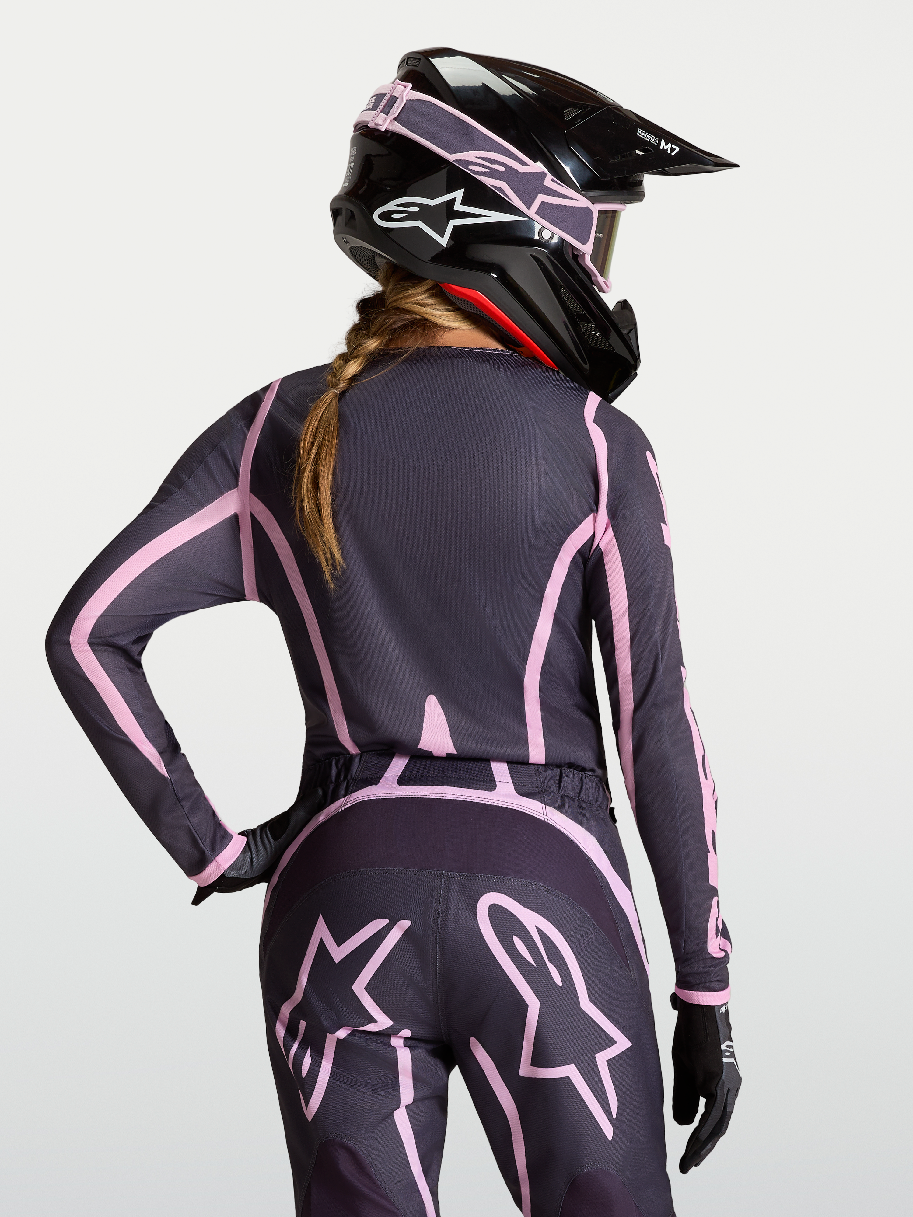 Alpinestars Camisola Stella Fluid Apex V2, camisola de motocross para mulher, cinzenta e rosa, vista traseira, com capacete a condizer.