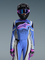 Piloto de motocross feminina a usar o conjunto de equipamento Alpinestars 2026 Stella Techstar Nomur, camisola azul com logótipo de estrela cor-de-rosa e roxo, calças azuis a condizer com painéis laterais brancos e pretos, capacete preto com óculos roxos e azuis, e luvas cor-de-rosa e pretas, kit completo de competição off-road para mulher