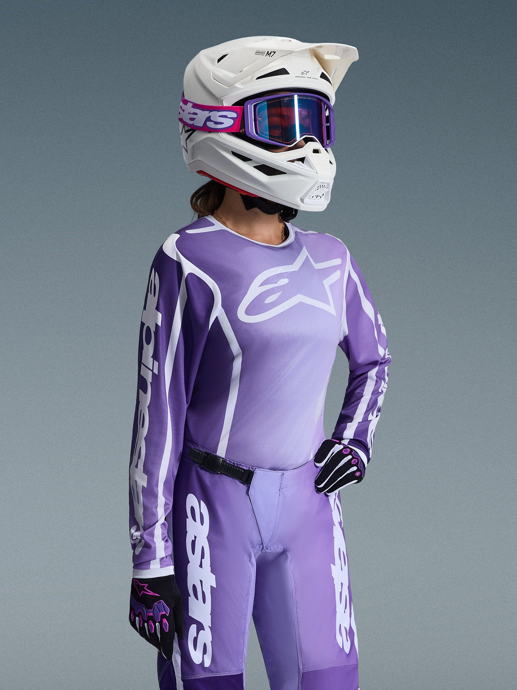 Conjunto de Equipamento Alpinestars Stella Fluid Apex Feminino 2026, camisola e calças de motocross em roxo e lavanda, usado por uma piloto com capacete branco e óculos roxos, apresentando logótipos Alpinestars brancos em destaque