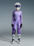 Piloto de motocross a usar o Conjunto de Equipamento Alpinestars Stella Fluid Apex 2026, camisola roxa com logótipo branco, calças roxas a condizer com marca branca, capacete branco com óculos cor-de-rosa, botas brancas e pretas, conjunto de motocross feminino coordenado para corridas todo-o-terreno
